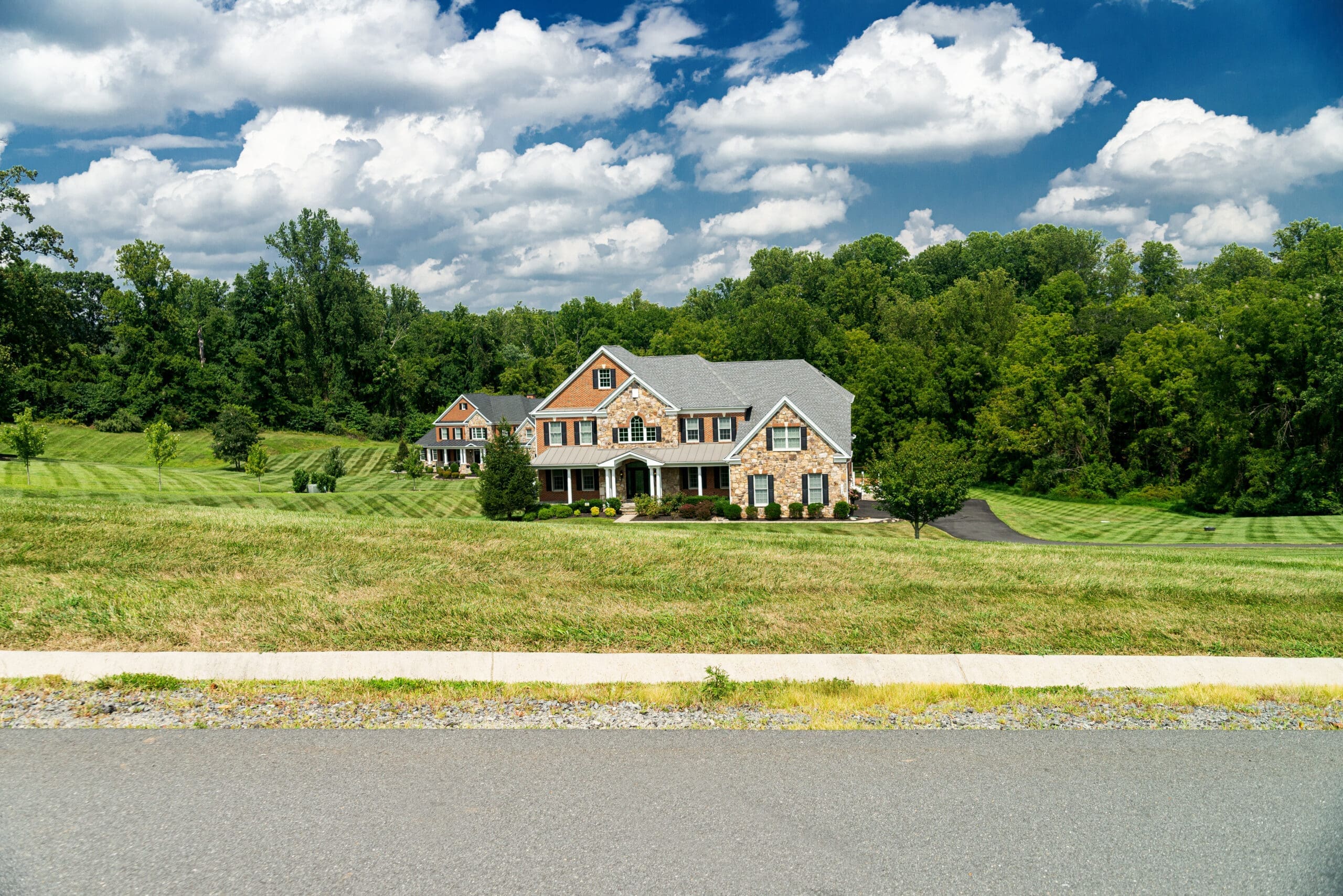 Leesburg. Virginia. USA. August 15, 2022. Large country brick house and summer landscape with a perfect lawn. Blue sky and white clouds.